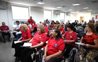 Grupo de hombres y mujeres de diversas edades, pacientes de Parkinson, integrantes del coro 'Voces que inspiran', en un salón del Hospital Rawson. Se los ve animados antes de su presentación por el Día Mundial del Parkinson."