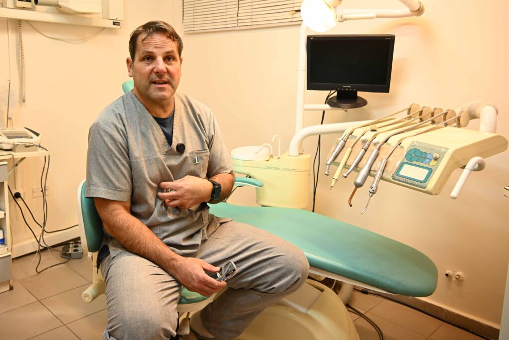El odontólogo Adrián Battezzati durante la entrevista, hablando, en su consultorio dental, con un sillón odontológico de fondo y equipamiento médico.